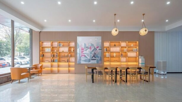 Un hall d’entrée spacieux au design moderne, comprenant une table centrale entourée de chaises, une grande peinture abstraite au mur et une bibliothèque avec des étagères éclairées.