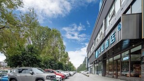 Un hôtel à la façade moderne, une rangée de voitures garées et des arbres bordant la rue.