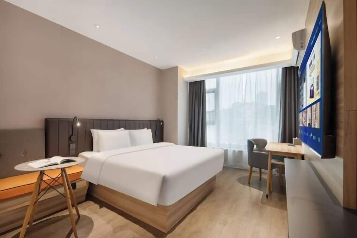 Una habitación de hotel con cama, escritorio, silla, una mesita y televisor.