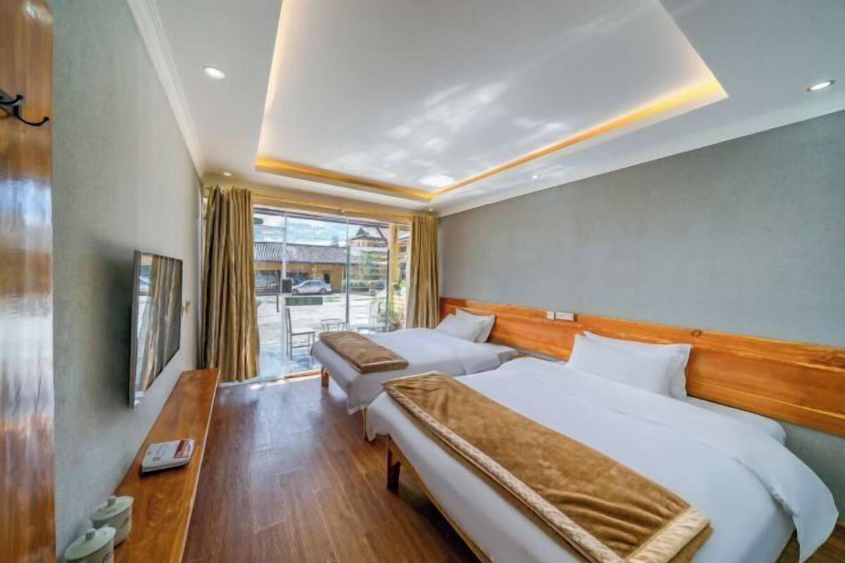 Une chambre d’hôtel avec deux lits, un banc en bois, une télévision et une vue sur l’extérieur.