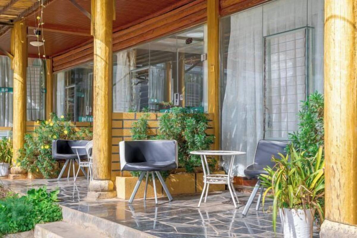 Un espace extérieur aménagé avec des piliers en bois, des chaises noires et une petite table ronde.