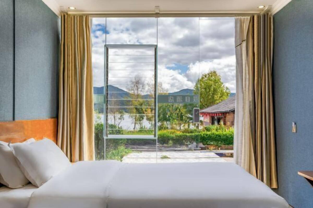 Une chambre d’hôtel avec un grand lit, des rideaux de couleur beige et une vue sur un bâtiment traditionnel et un espace verdoyant.