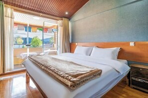 A hotel room with a large bed, wooden headboard, and a view through a sliding glass door to an outdoor area.