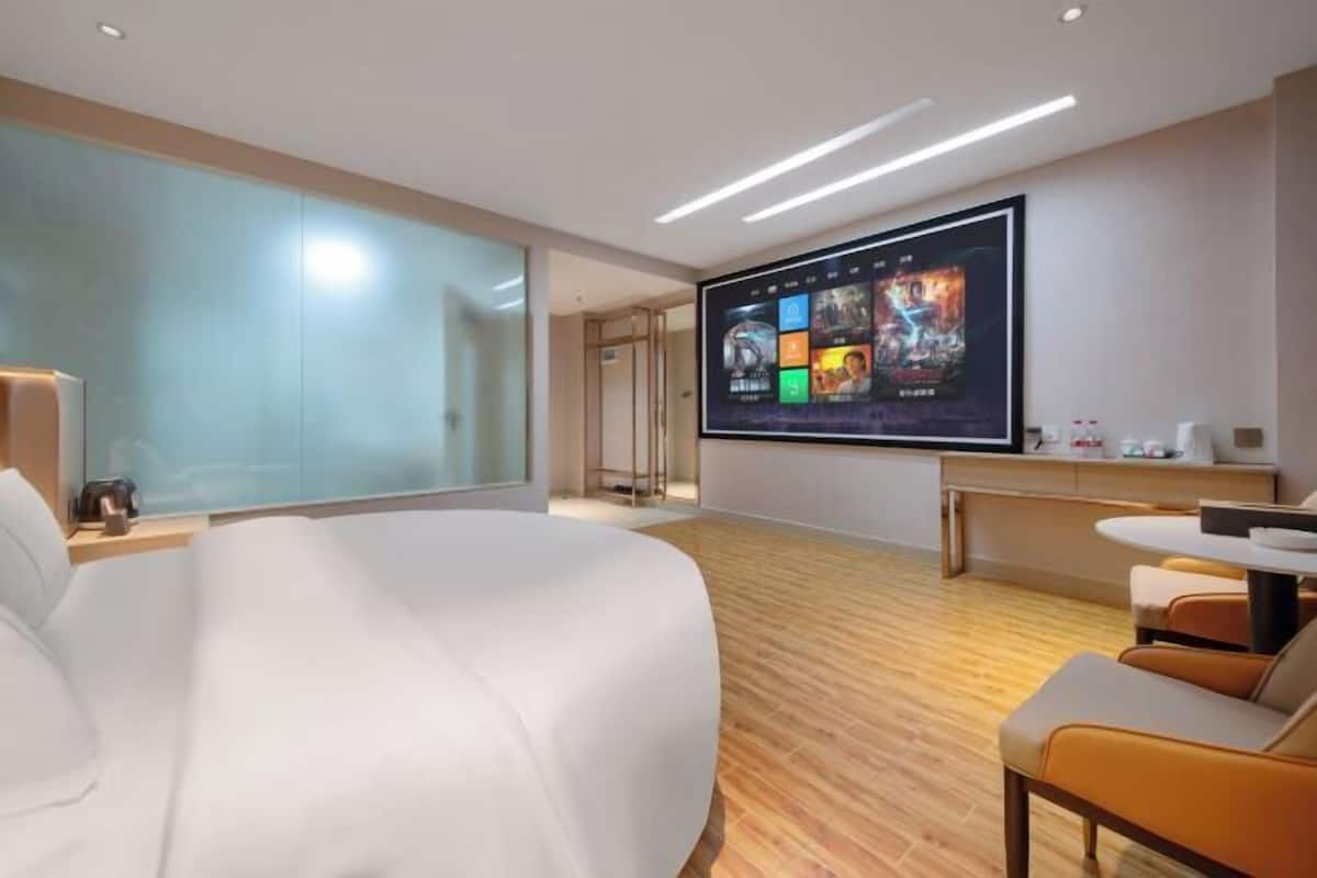 Una habitación de hotel moderna con una cama grande, un escritorio con televisor de pantalla plana y una zona de estar con sillones.