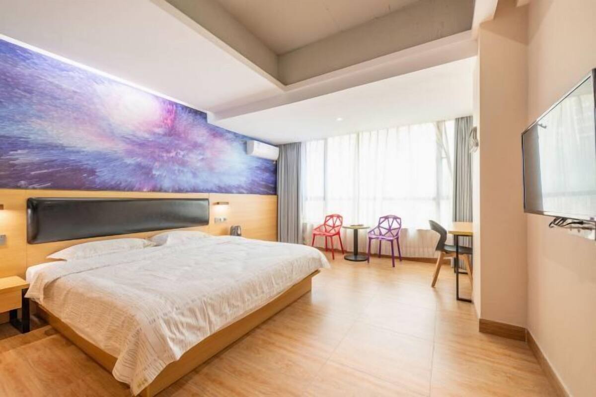 Moderni hotellihuone, jossa on suuri sänky, taulu seinällä, työpöytä tuoleineen ja televisio.