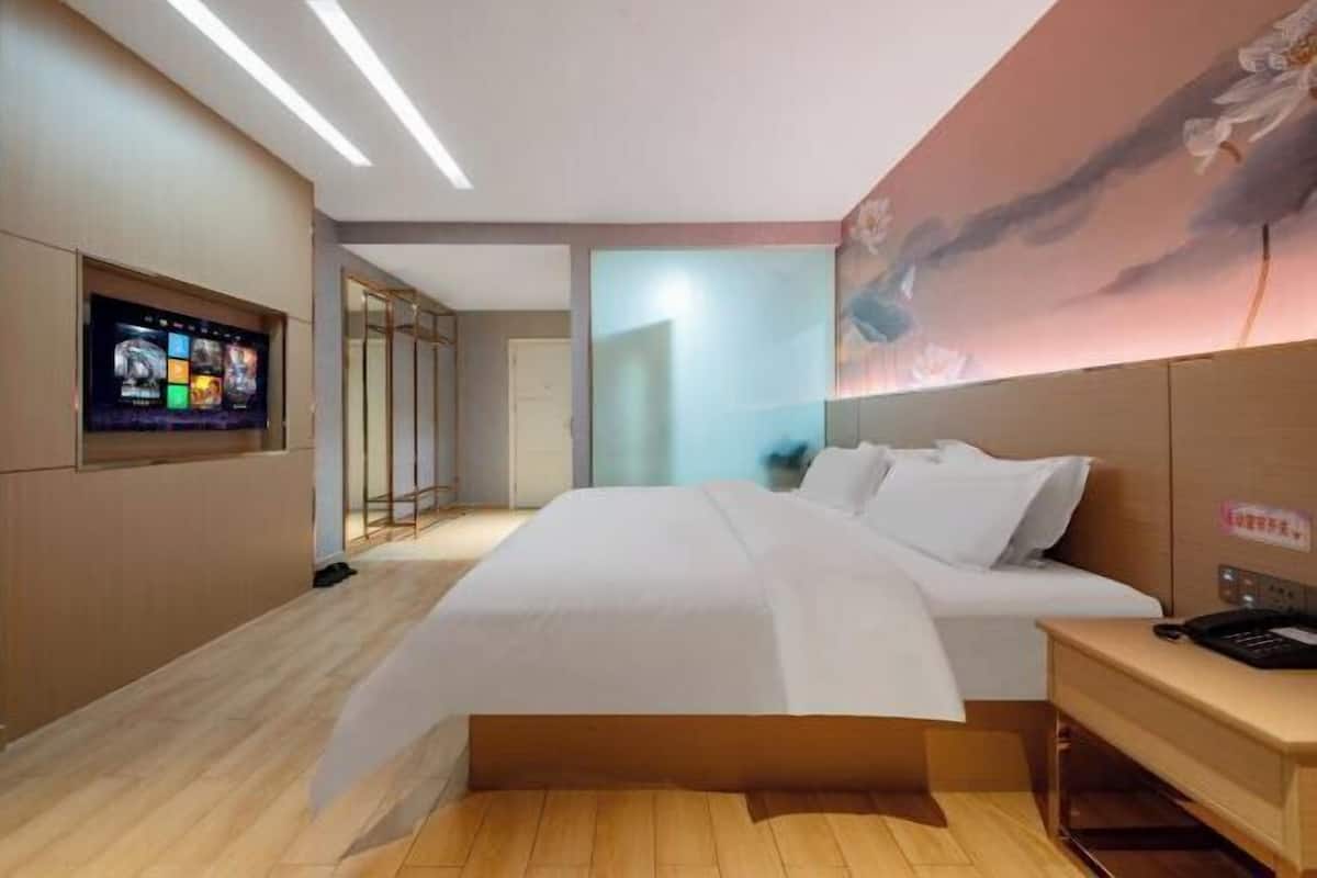 Moderni hotellihuone, jossa on suuri sänky, seinälle asennettu taulutelevisio ja puulattia.