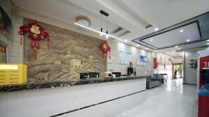 Zona de recepción de un hotel con mostrador de mármol, detalles decorativos rojos y un mural de un castillo.