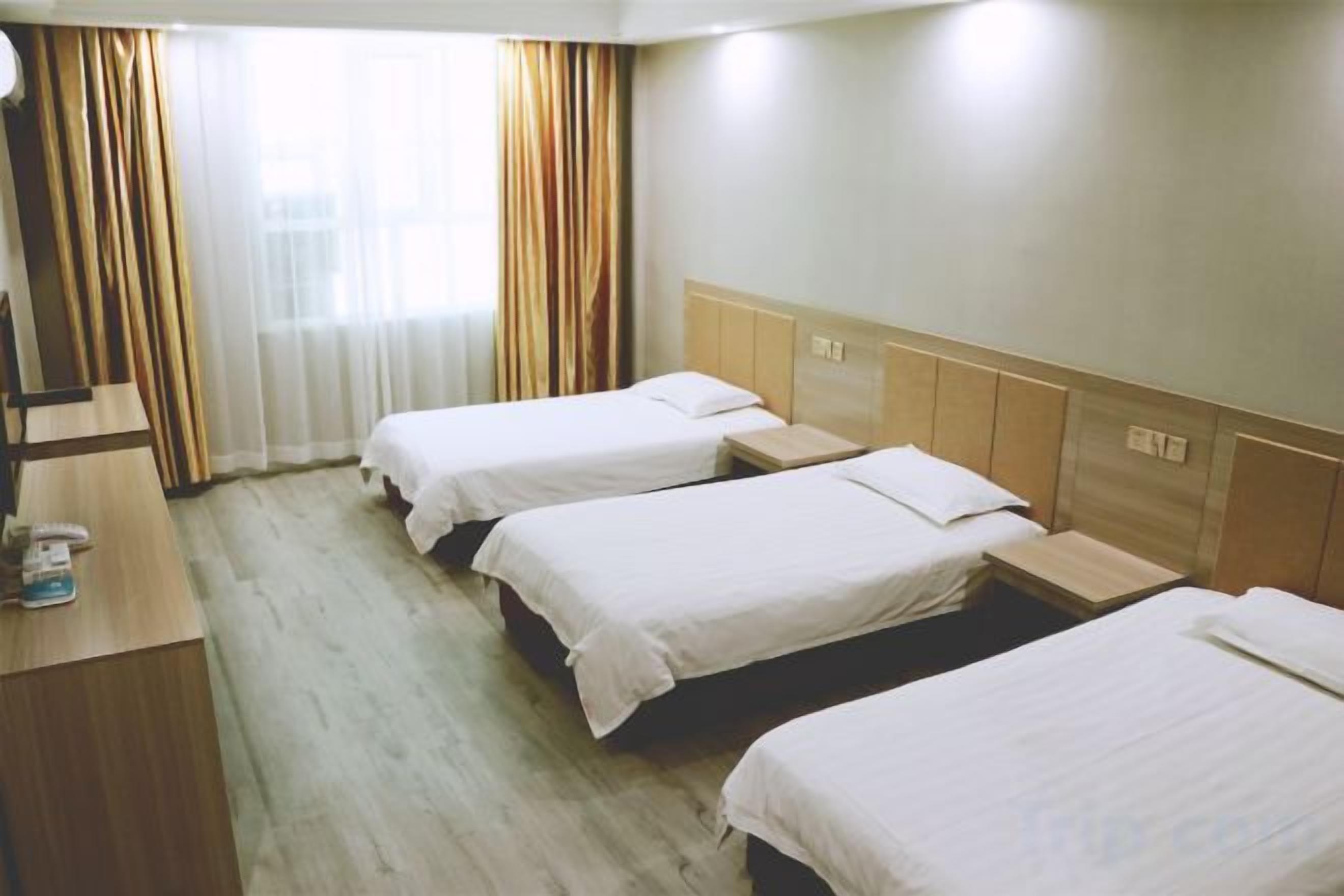 A hotel room with three beds, a desk, and a window with curtains.