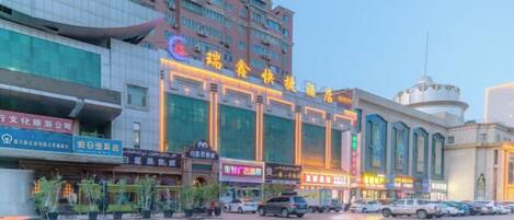 A multi-story hotel with a prominent entrance and signage, a parking lot with several cars, and a clear sky.