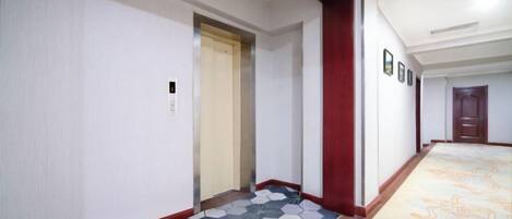 A hotel corridor with a patterned carpet, a door, and a wall-mounted sign.