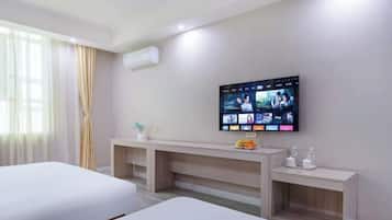 Habitación de hotel con dos camas, un televisor instalado en la pared mostrando varios canales, una mesita con un frutero y una mesita de noche con artículos de aseo.