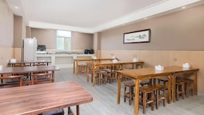 Un amplio comedor con varias mesas y bancos de madera, una cocina al fondo y un cuadro en la pared.