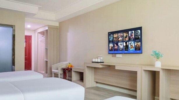Habitación de hotel con dos camas, un televisor montado en la pared, una mesita con un florero y una puerta roja al fondo.