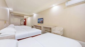 Habitación de hotel con tres camas, un escritorio, una silla y aire acondicionado.