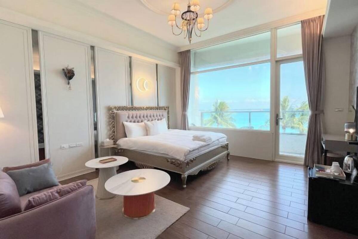 A bedroom with a large bed, a chandelier, a view of the sea, and a balcony.
