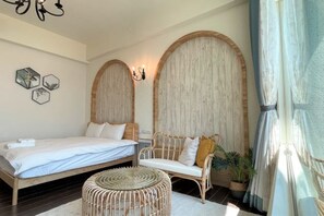 A bedroom with a bed, a white sofa, a round wicker ottoman, and a wall with a wooden panel design. - Angel Inn (Hualien)