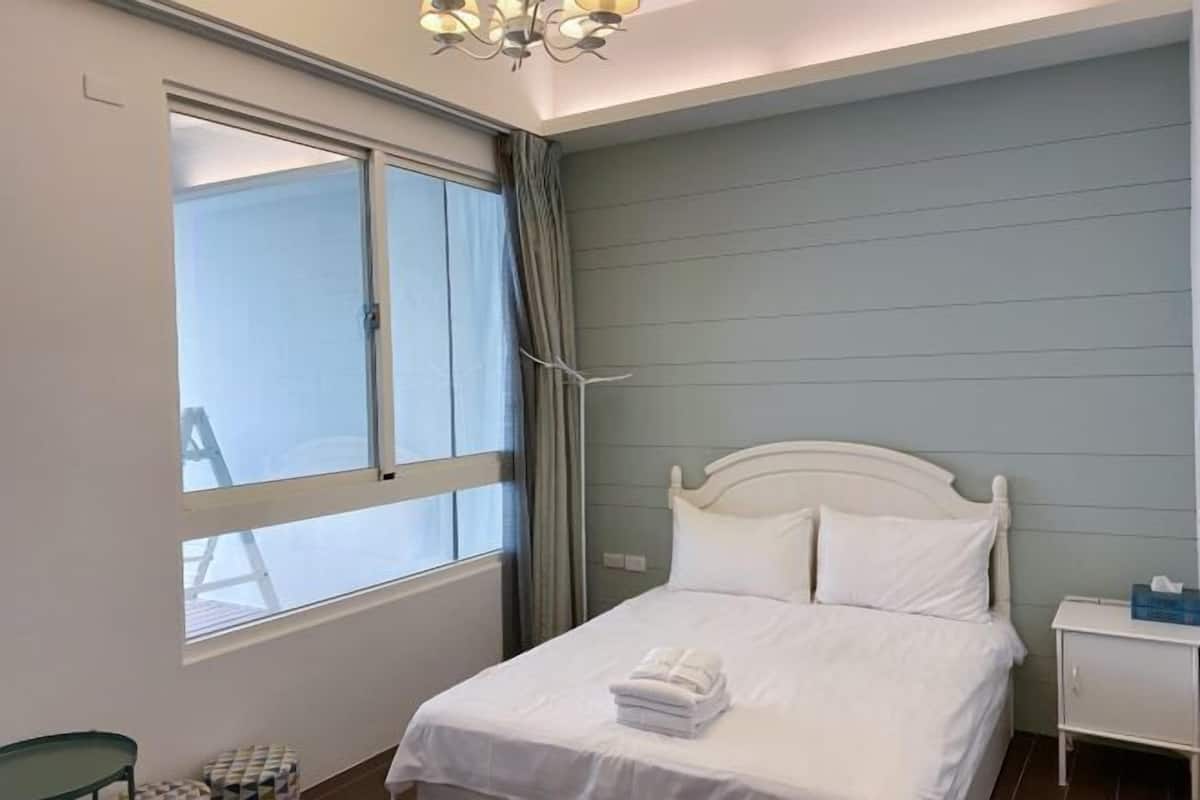 A bedroom with a bed, a nightstand, a window with curtains, and a chandelier.