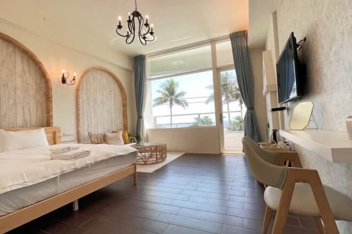 A hotel room with a bed, a desk, a TV, and a view of palm trees.