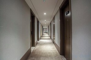 Pitkä, kapea hotellikäytävä, jossa on ovet molemmilla puolilla, matto lattialla ja upotetuilla valaisimilla varustettu katto.