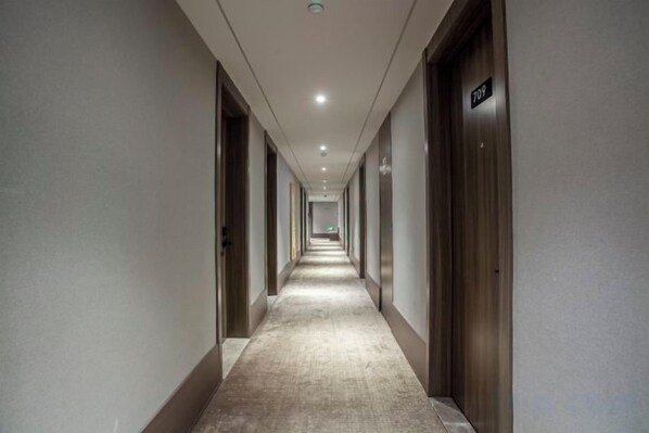 A long, narrow hotel corridor with doors on both sides, a carpeted floor, and a ceiling with recessed lighting.