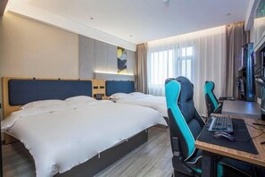Hotellihuone, jossa on kaksi sänkyä, työpöytä tietokoneella sekä suuri ikkuna, jossa on verhot.