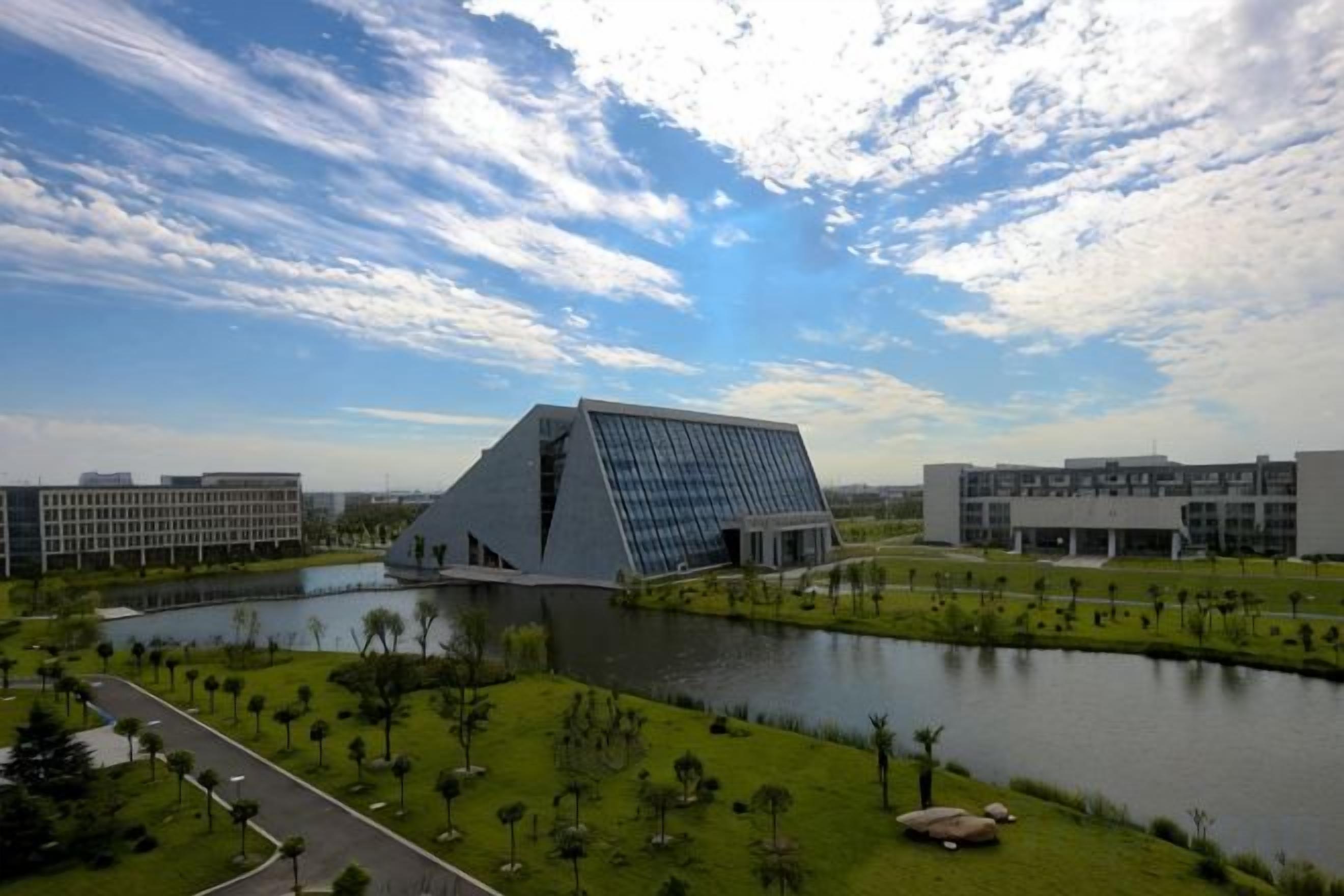 Un edificio moderno con un techo triangular distintivo, rodeado de agua y vegetación.