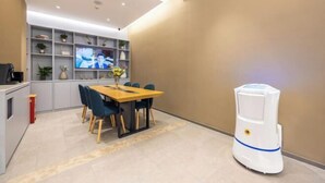 A modern dining area with a wooden table and chairs, a TV mounted on the wall, and a robot vacuum cleaner. - Homeinn · neo (Jiuquan West Street Bus Station) (Jiuquan)
