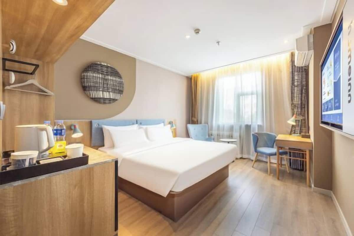 A hotel room with a bed, desk, chair, and a wall-mounted TV.