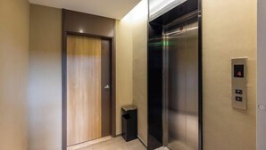 A modern elevator with a digital display showing the number 4, a trash bin, and a wooden door. - Homeinn · neo (Jiuquan West Street Bus Station) (Jiuquan)