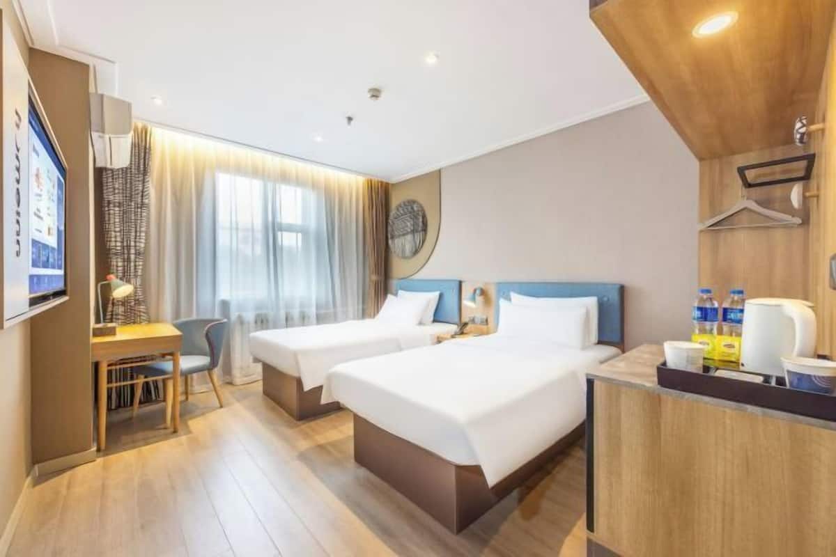 A hotel room with two beds, a desk, a chair, a TV, and a wooden reception desk.