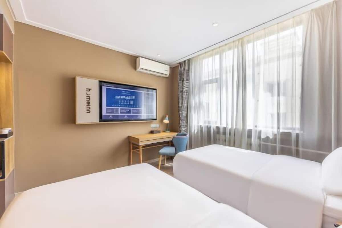 A hotel room with two beds, a desk, a chair, a TV, and a window with curtains.