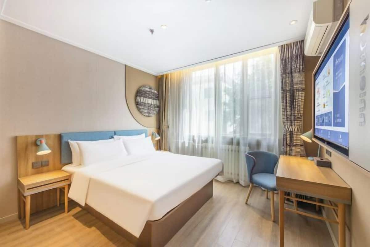 A hotel room with a bed, a desk, a chair, a TV, and a window with curtains.