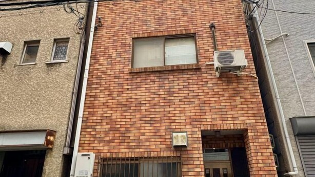 A brick building with multiple windows, some with shutters, and an air conditioning unit mounted on the wall. - Japanese Cottage Kenkou (Osaka)