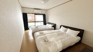 A hotel room with two beds, a window with curtains, a ceiling light, and a visible brick wall outside. - Japanese Cottage Kenkou (Osaka)