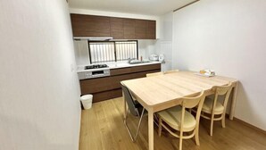 A compact kitchen with a dining table and chairs, a window with blinds, and a white sink. - Japanese Cottage Kenkou (Osaka)
