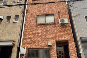 A brick building with a small window and an air conditioning unit mounted on the wall. - Japanese Cottage Kenkou (Osaka)