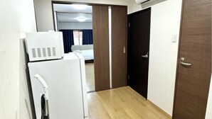 A compact hotel room with a refrigerator, a wooden wardrobe, and a sliding door leading to a bathroom. - Japanese Cottage Kenkou (Osaka)