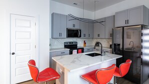A modern kitchen with grey cabinets, a stainless steel refrigerator, a microwave, and a sink. There are three red chairs around the island. - Modern 2Bedroom house in Dallas with WiFi (Dallas)