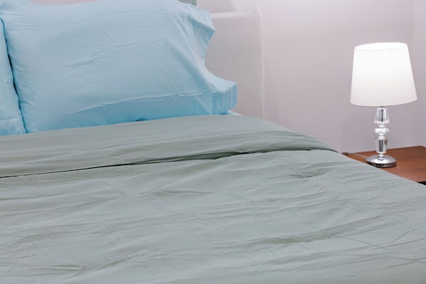 A bed with a grey bedspread and a white lamp on a wooden nightstand.
