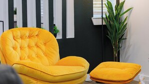 A yellow tufted armchair and ottoman in a room with black and white striped walls, a potted plant, and a window with blinds. - Modern 2Bedroom house in Dallas with WiFi (Dallas)