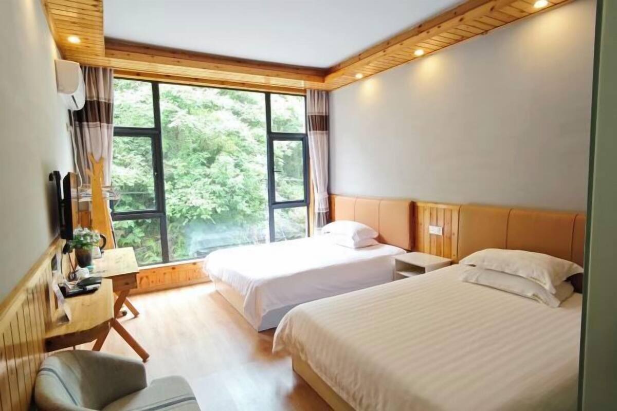 A bedroom with two beds, a desk, a chair, and a large window.