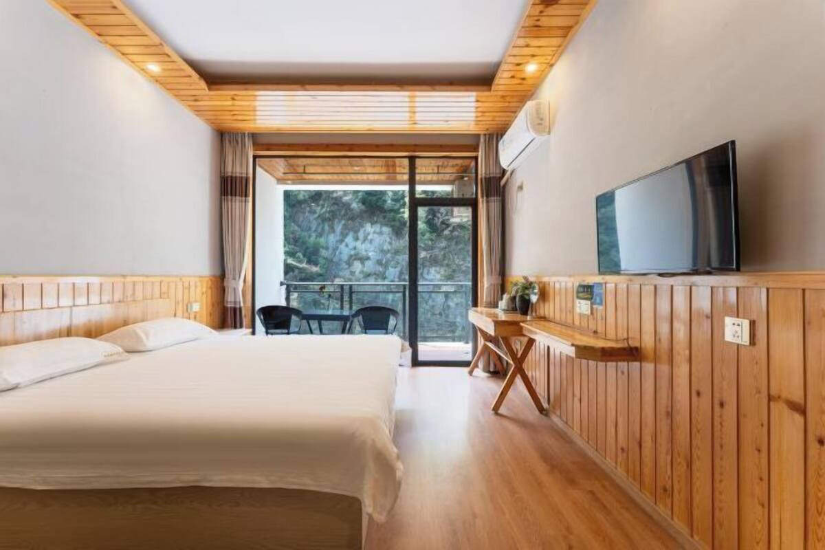 A bedroom with a bed, a TV, a desk, and a window with a view of trees.