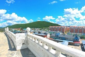 Ein weißer Balkon mit Balustrade, der auf eine Stadt mit Gebäuden und einer Hügelkulisse blickt.