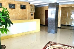 Un espace d’accueil avec un comptoir de réception, une plante en pot, une horloge et une porte en arrière-plan.