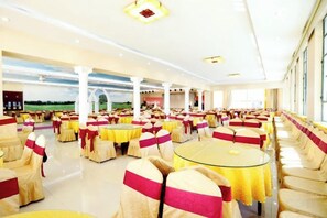 Une salle de banquet avec des tables et des chaises rondes, de grandes fenêtres et une vue sur l’extérieur.