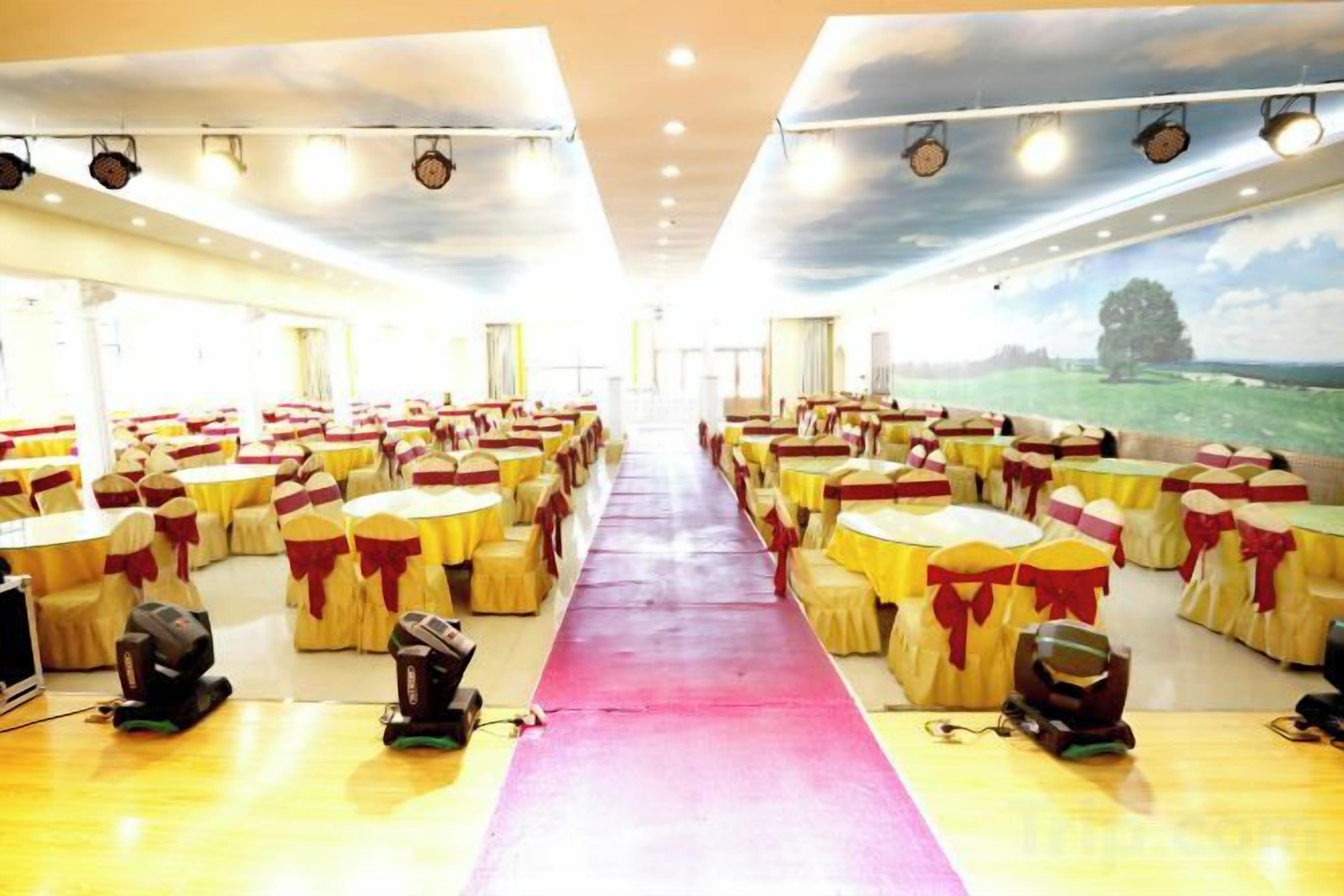 A banquet hall with rows of tables and chairs, a central aisle, and a view of a landscape through the windows.