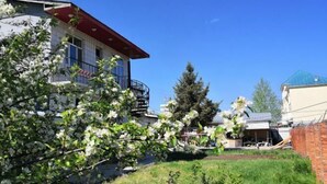 Un edificio residencial con balcón, un jardín lleno de flores y un cielo azul despejado.