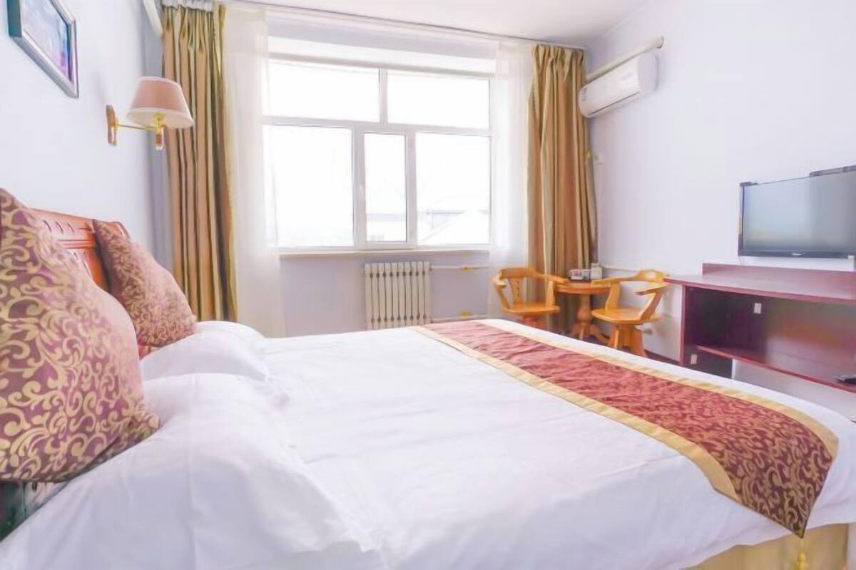 Een hotelkamer met een groot bed, een bureau met stoel, een televisie en een raam met gordijnen.