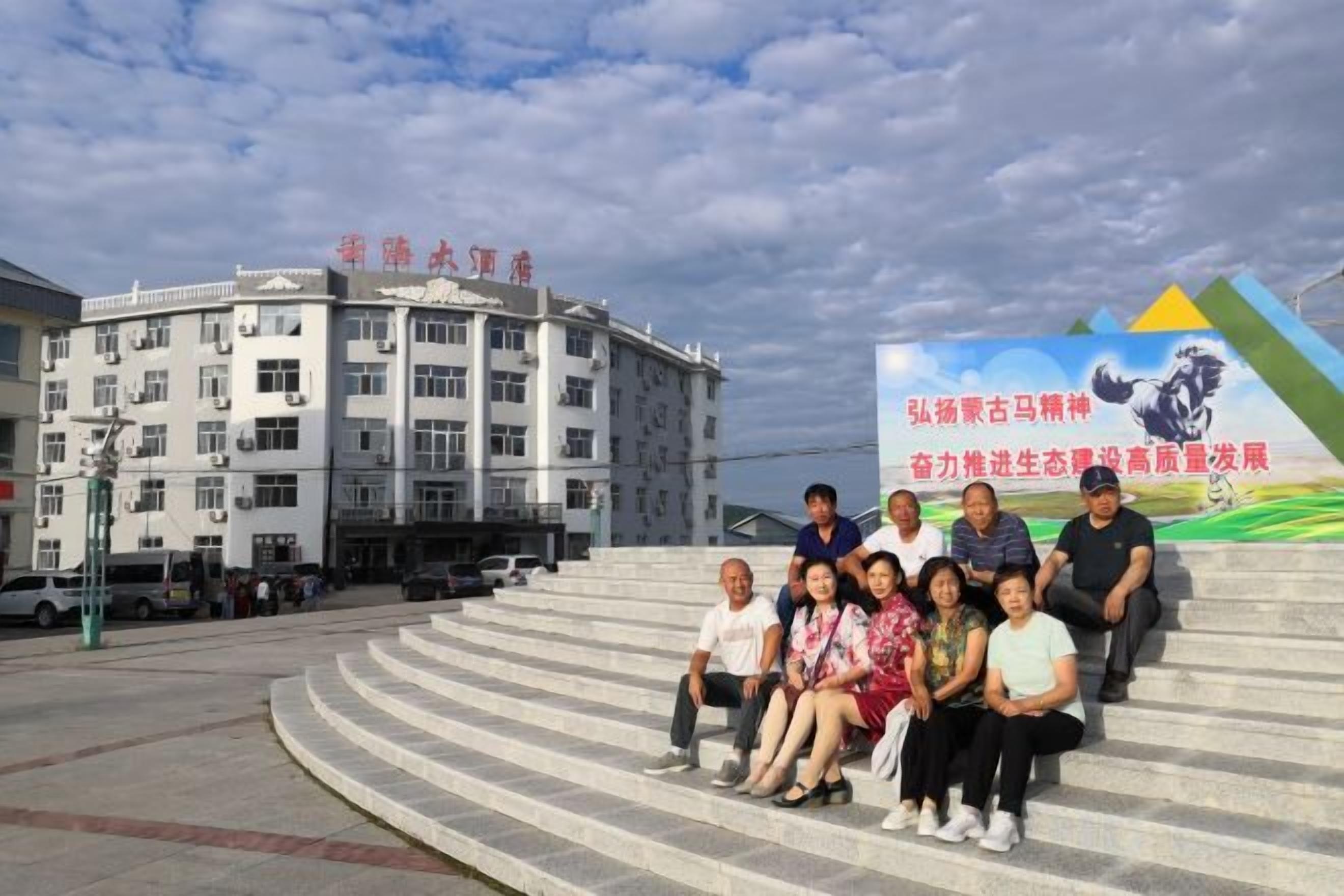A group of people seated on outdoor steps in front of a building with a large sign.