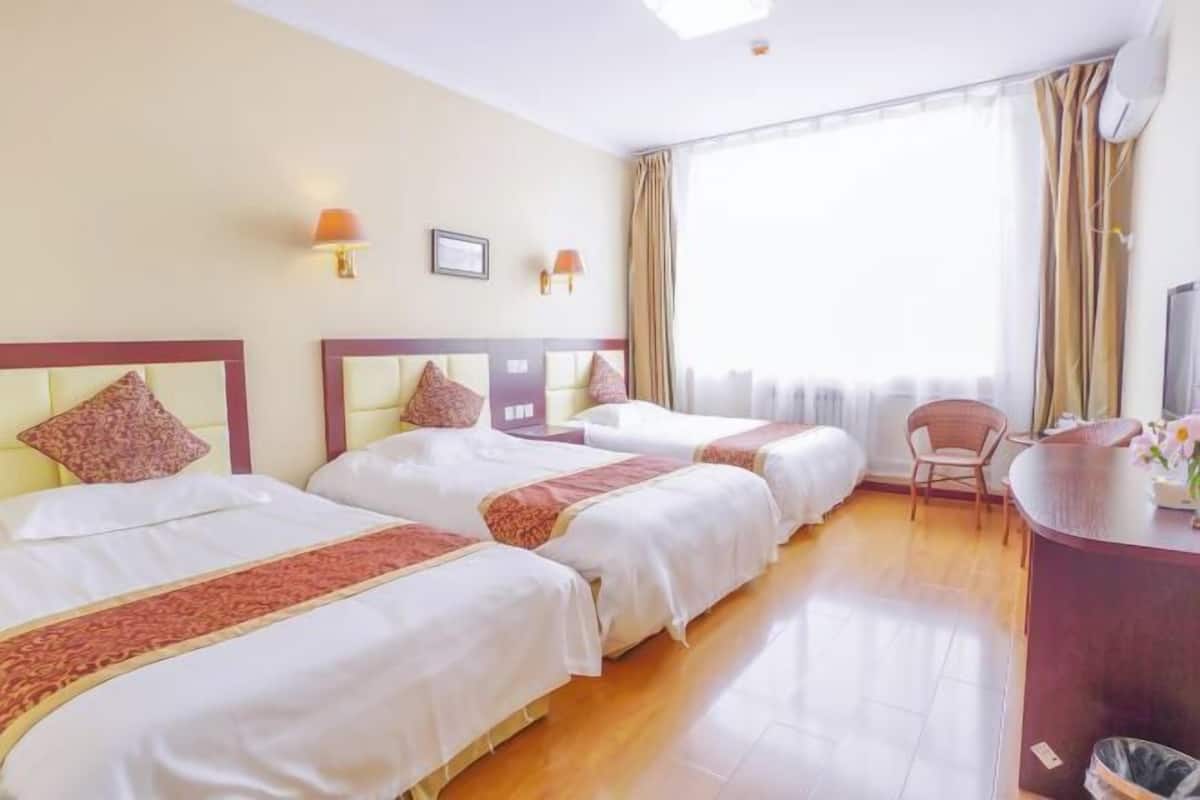 Een hotelkamer met twee bedden, een bureau, een stoel en een groot raam met gordijnen.